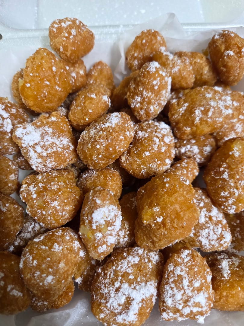 Close-up of golden-brown fried dough balls, generously dusted with powdered sugar, in a white container.