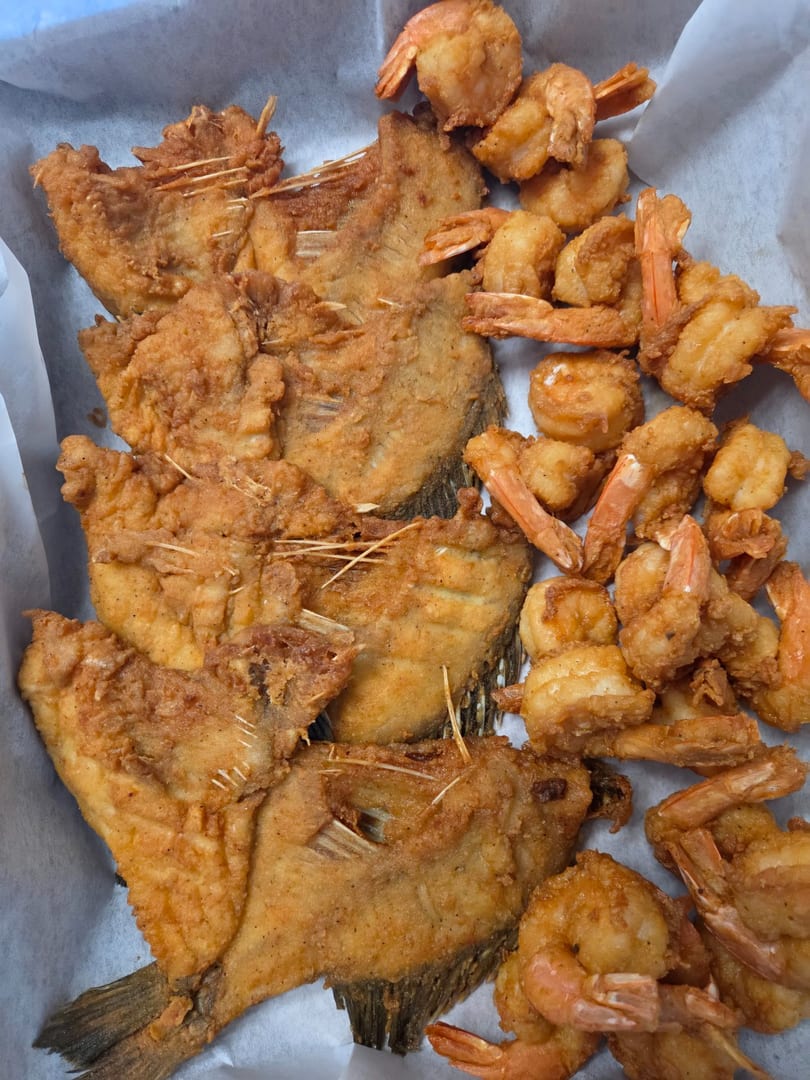 Crispy fried whole fish and shrimp arranged on white parchment paper.