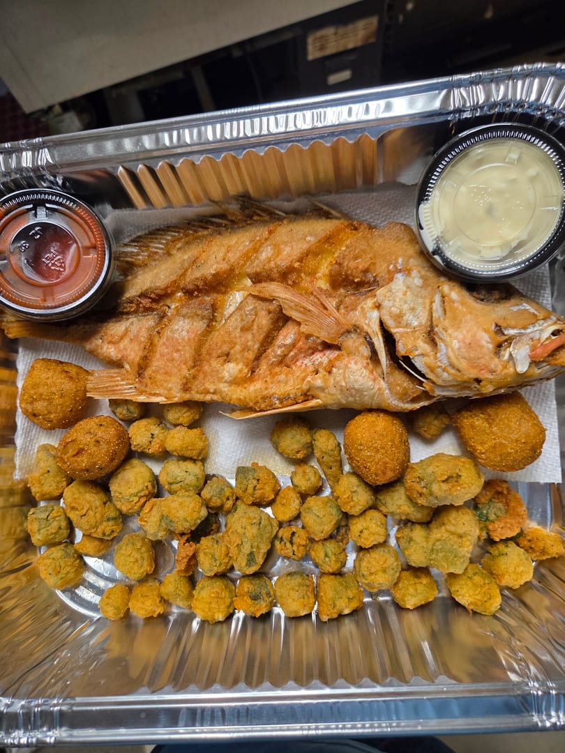 Fried whole fish, hush puppies, and fried okra with dipping sauces in a foil takeout container.