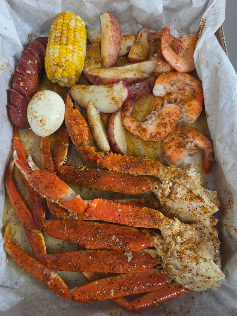 Seafood boil with crab legs, shrimp, sausage, corn, potatoes, and a hard-boiled egg in a paper-lined tray.