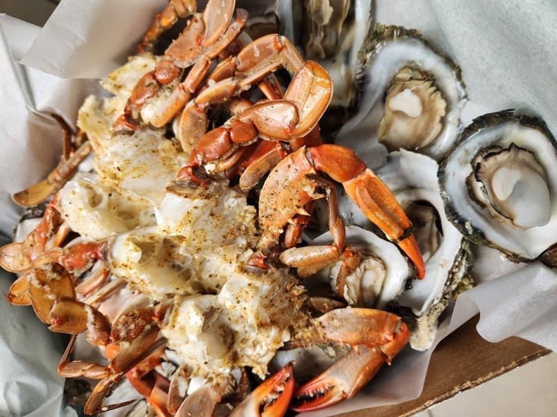 Steamed blue crabs with seasoning and fresh oysters in a box lined with white paper.