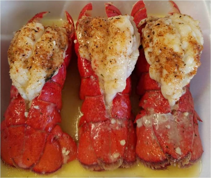 Three seasoned lobster tails with drawn butter, presented in a white dish.