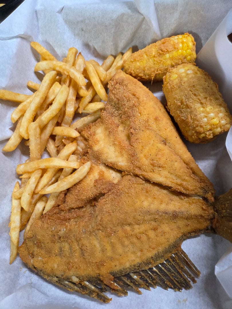 Fried fish fillets with french fries and two corn on the cob pieces in a paper-lined basket.
