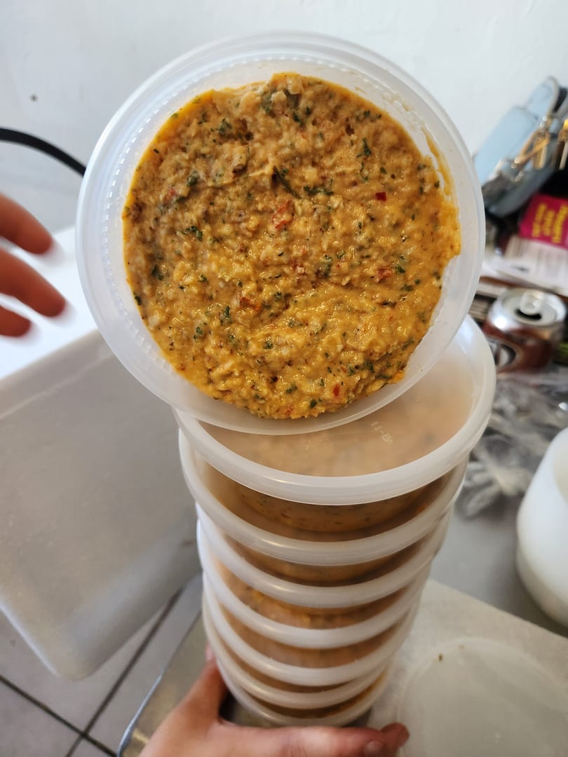A stack of clear plastic containers filled with a textured orange dip, garnished with green herbs.