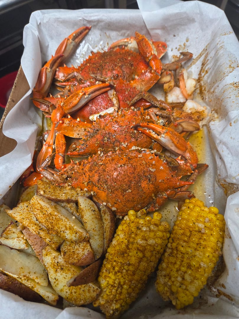 Boiled crabs, seasoned potato wedges, and corn on the cob in a paper-lined box.