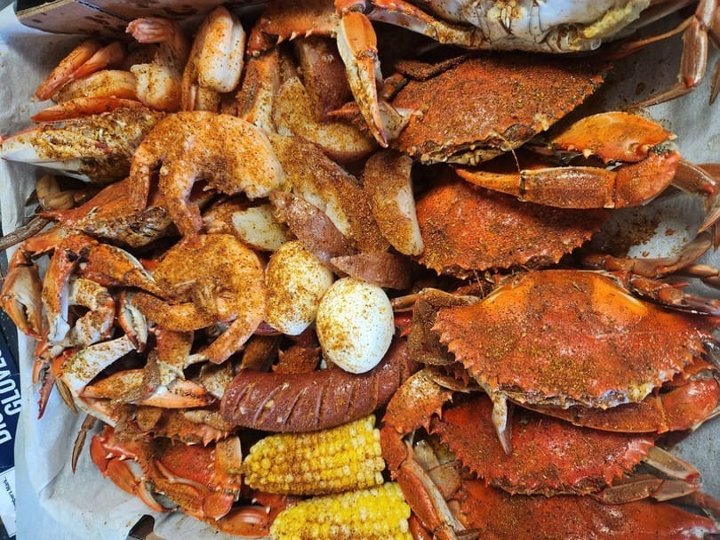 A seafood boil with crabs, shrimp, corn on the cob, potatoes, sausage, and eggs.